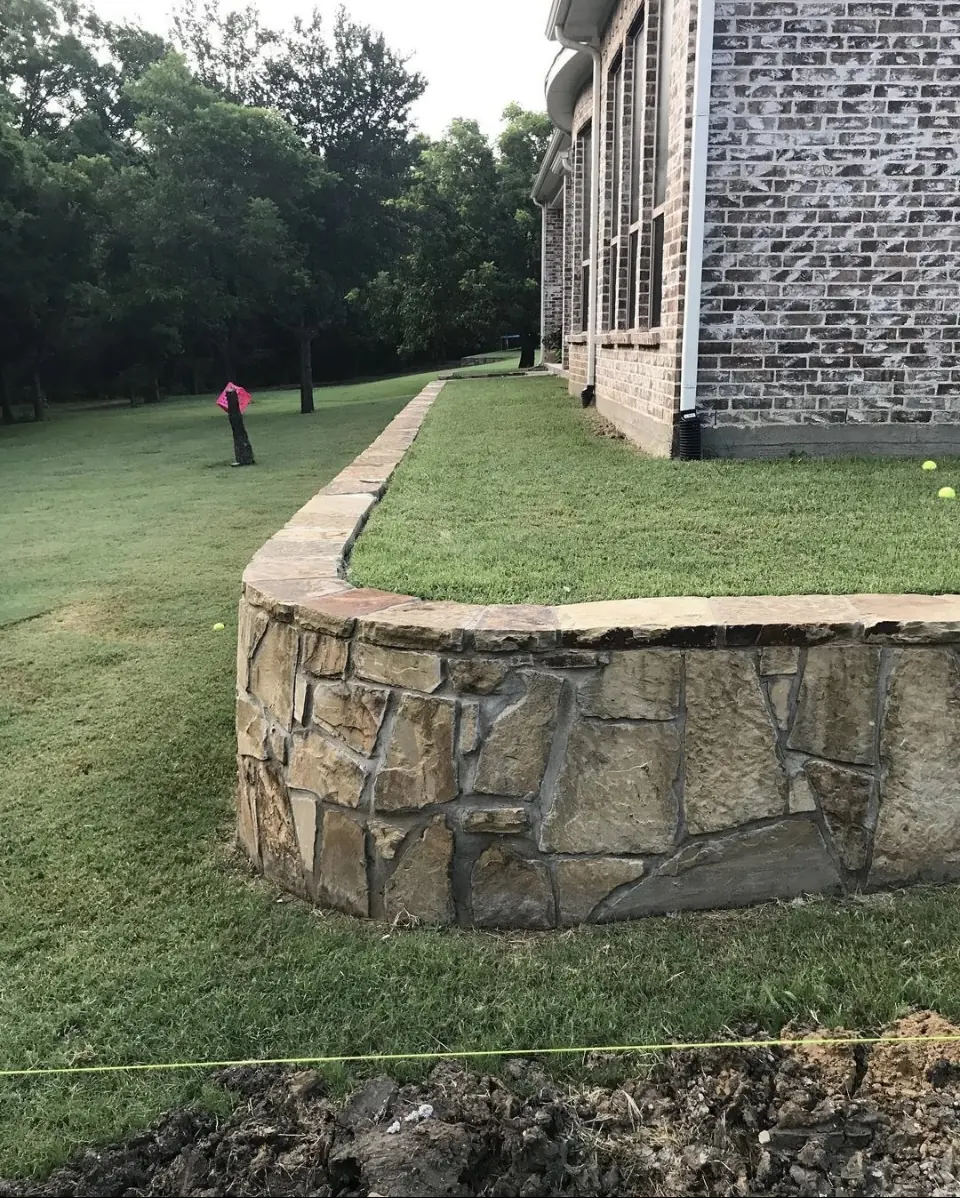 Curved natural stone retaining wall beside a home
